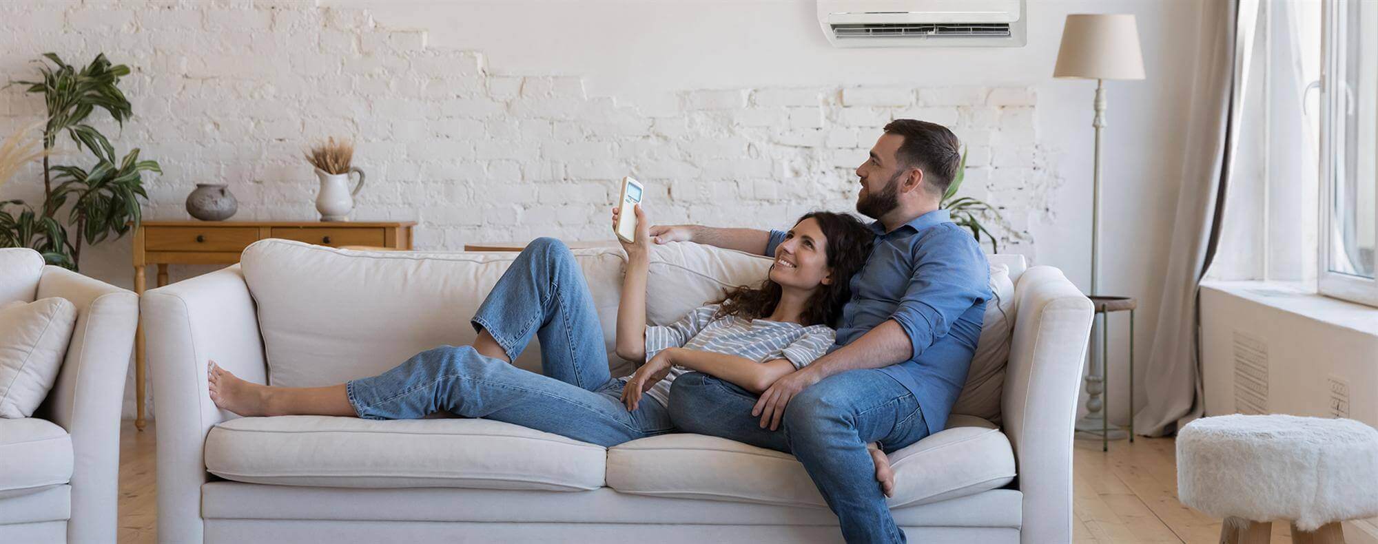 A couple relaxing on a sofa with effective heating and cooling, enjoying clean air from the properly maintained HVAC system. The system includes aeroseal duct sealing to ensure optimal efficiency and comfort. The importance of regular duct cleaning and air quality testing is highlighted to prevent issues and maintain an energy-efficient environment. Boiler repair and furnace maintenance are part of the overall service plan to ensure long-lasting performance and consistent temperature control.