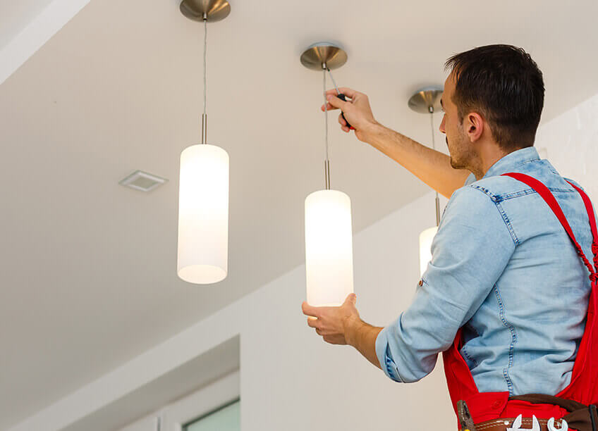 A person replacing a light fixture in a home, representing electrical work and home maintenance services, including lighting repair. This image is a great fit for showcasing home improvement solutions like electrician services, HVAC systems, furnace replacement, boiler repair, and ductwork installation. Ideal for content focused on electrical contractor work, home energy systems, and other residential services like AC repair and home lighting upgrades.